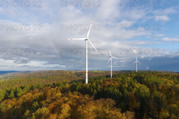 Wind turbines rise above an autumnal forest with a rainbow in the background, near Schorndorf,