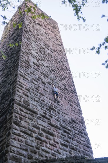 A climber climbs the stone wall of a tower, accentuated by clear air and natural surroundings,