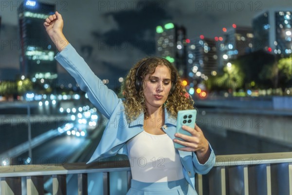 Young woman with curly hair wearing headphones and an elegant blue outfit, expressing joy and
