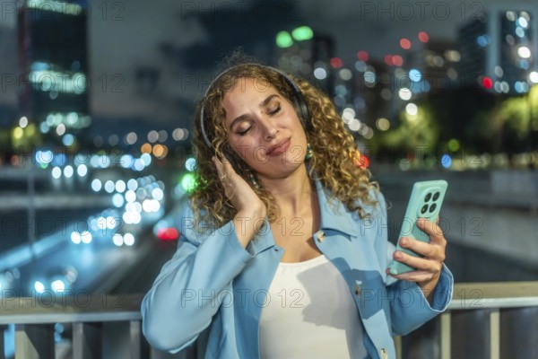 Young woman with curly hair finding joy and relaxation listening to music using headphones and a