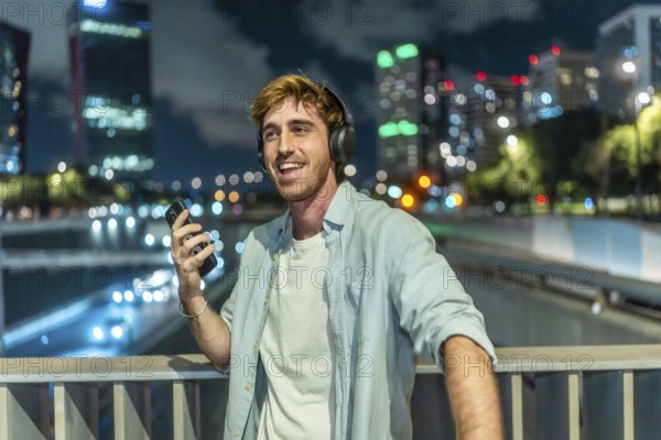 Smiling young man wearing headphones and holding a smartphone, happily listening to music while