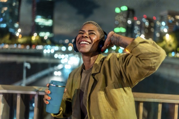 Smiling woman listening to music with headphones, adjusting an earcup, and holding a reusable