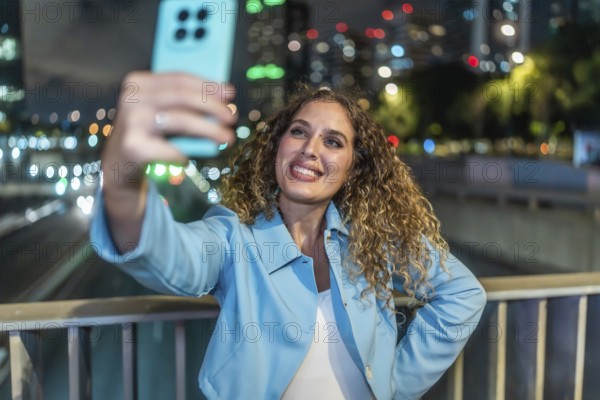 Young woman with curly hair smiling happily while capturing a selfie on her mobile phone, standing