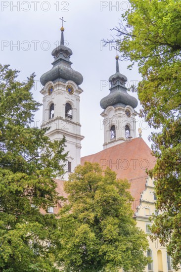 Two decorative church towers rise above a red roof surrounded by green trees, ZFP Zwiefalten,