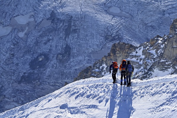 Three ascended mountaineers run across a snow-covered mountain ridge, Aiguille du Midi,