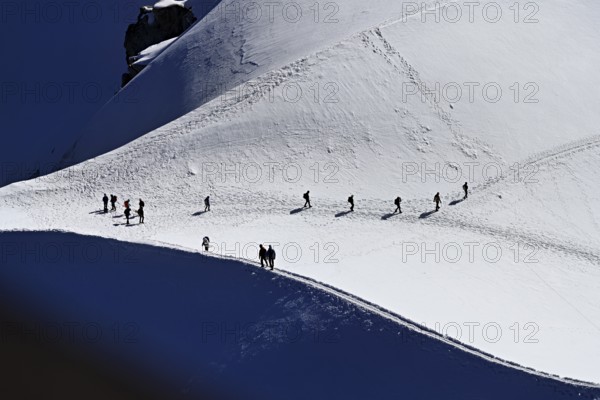 A group of mountaineers runs across a snow-covered mountain, Aiguille du Midi, Chamonix-Mont-Blanc,