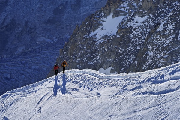Two ascended mountaineers run across a snow-covered mountain ridge, Aiguille du Midi,