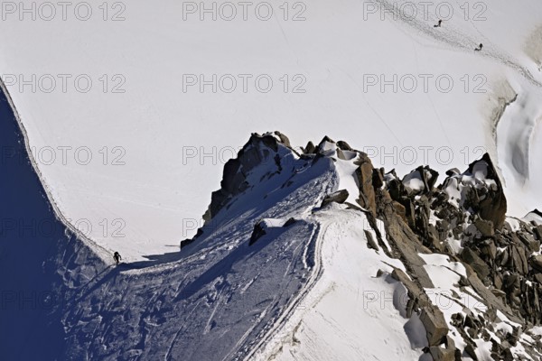 A mountaineer climbs over a snow-covered mountain ridge, Aiguille du Midi, Chamonix-Mont-Blanc,