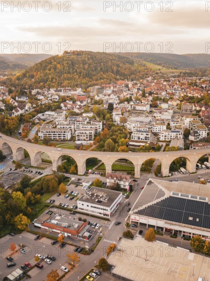 Aerial view of the city with an elongated bridge surrounded by autumn trees, hills and an urban