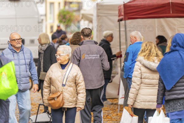 People wearing autumn clothes visit a market while the ground is covered with leaves,