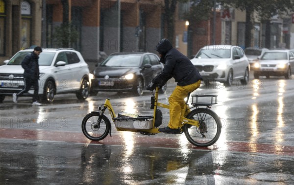 A man rides a cargo bike across a rained road in heavy rain, Berlin, 30.10.2025, Berlin, Berlin,