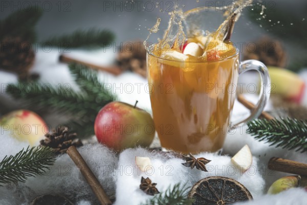 Apple punch splashes out of a glass cup with apple pieces, surrounded by cinnamon sticks and pine