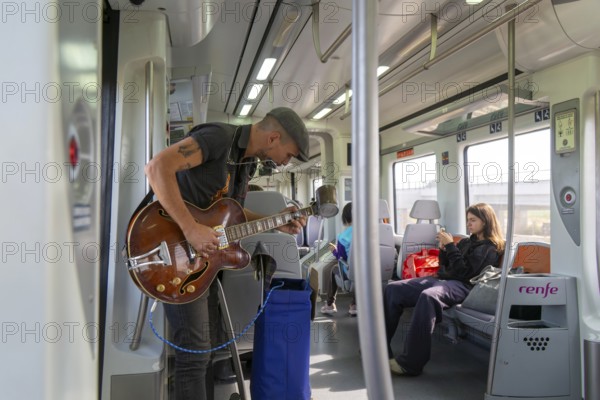 Musician busker playing guitar onboard train of Rodalia de Barcelona suburban rail network,