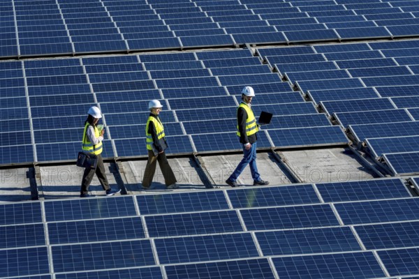 Three engineers walking on a rooftop solar power station, checking and inspecting the large array