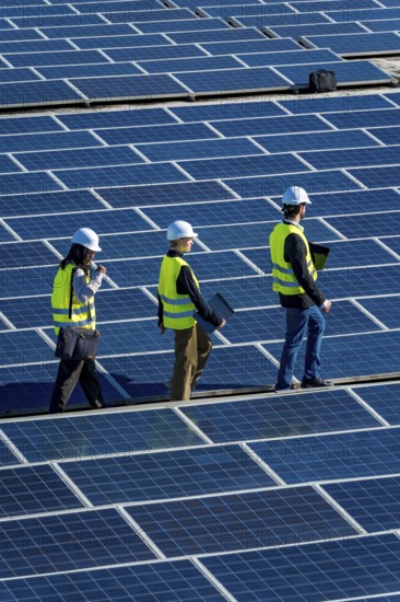 Engineers wearing safety vests and hard hats are walking across a vast array of solar panels at a