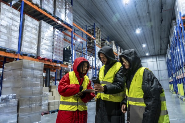 Diverse team in cold storage gear and high visibility vests using barcode scanner and tablet to
