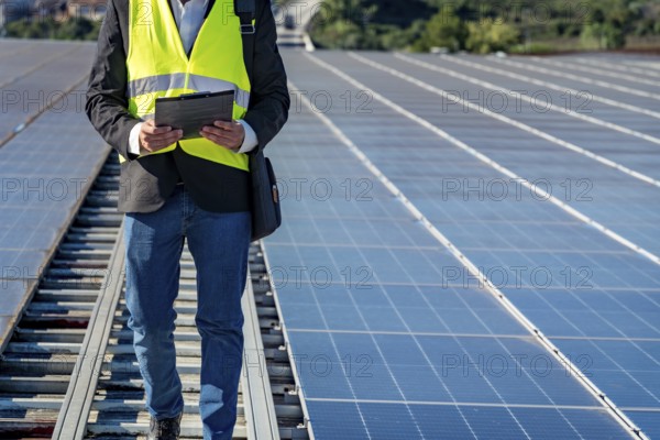 Technician working on a large solar panel installation, reviewing data on a clipboard while walking