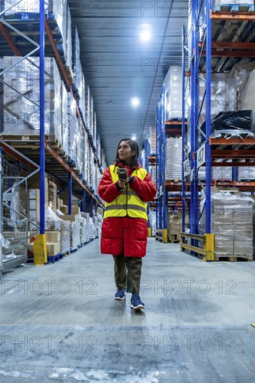 Woman wearing warm jacket and safety vest scanning inventory with a barcode reader, managing stock