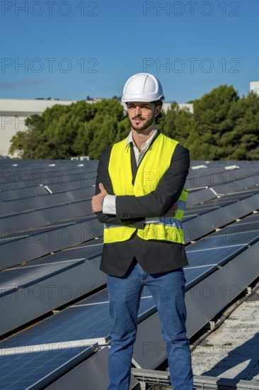 Engineer wearing a hard hat and safety vest standing confidently with arms crossed on a rooftop