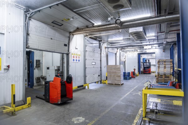 Industrial cold storage facility featuring multiple loading docks with pallet jacks and forklifts,