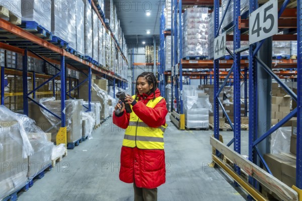 Woman worker in high visibility vest and warm jacket scanning pallets of boxes in a cold storage