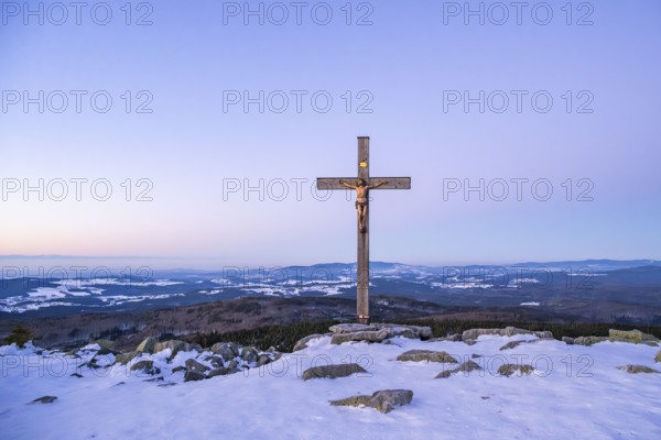 Christian cross on the peak of Mount Lusen with the view over the hills of the bavarian forest at