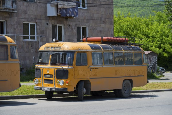 A vintage bus in orange with roof luggage, parked on a street against a green background, PAZ-672,