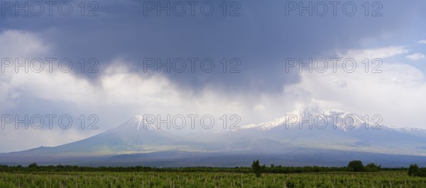 Two snow-capped mountains under dramatic skies with dark clouds over vast fields, Ararat and Little