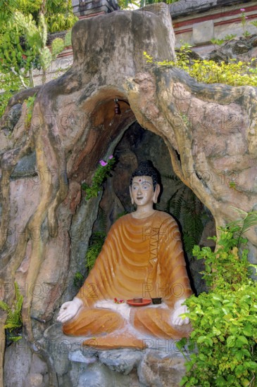 Statue figure of sitting Buddha in artificial grotto with hands shaped into thumb and index finger
