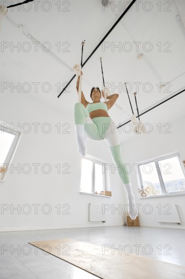 A fitness enthusiast practices stretching techniques with a hammock in a bright and airy indoor