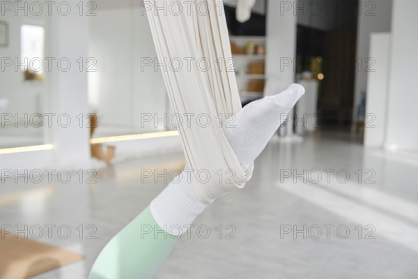 A person engages in fitness stretching using a hammock for support. The scene is set in a bright