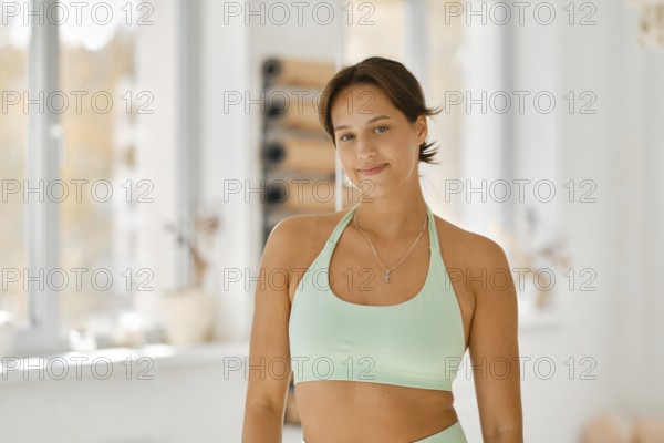 A woman wears a light green workout outfit while smiling in a well-lit fitness studio. The space