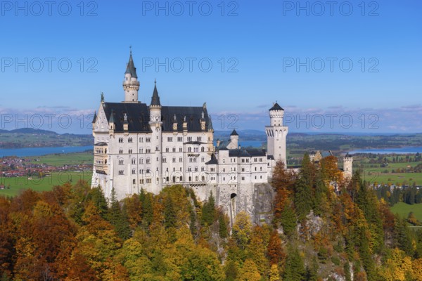 Impressive Neuschwanstein Castle in autumn landscape, surrounded by colorful trees and under blue