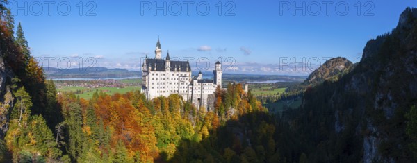 Neuschwanstein Castle towers over colorful forests in a vast landscape with blue skies, Schwangau,