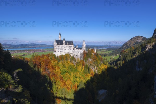 The impressive Neuschwanstein Castle surrounded by colorful autumn trees and a vast landscape,