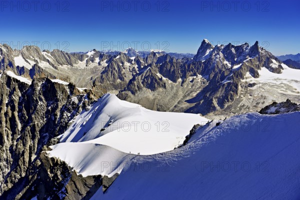 Mountaineers climb over a snow-covered ridge with Grandes Jorasses mountain in the background,