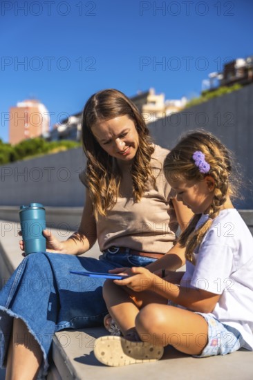 Mother and daughter smiling, sitting together on steps enjoying time outdoors, holding a reusable