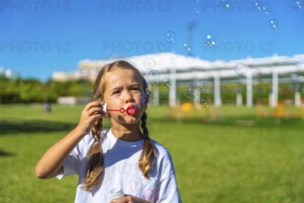 Child with pigtails enjoying summer playtime outdoors, actively creating and watching soap bubbles