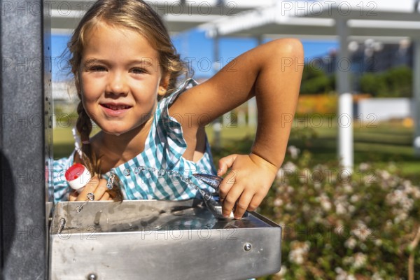Young child refreshing herself with a drink of water from a public fountain in a sunny park,