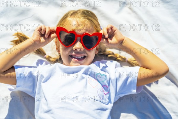 Young child lying outdoors on a white blanket, expressing joy and playing with vibrant red heart