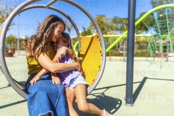Mother and daughter share a warm hug and bright smiles on a sunny playground, enjoying playful