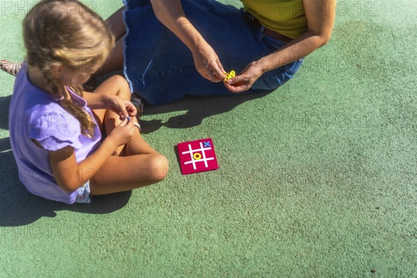 Mother and daughter bonding over a game of tic tac toe on a sunny day, enjoying quality family time
