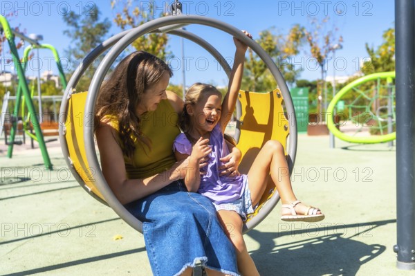 Mother and daughter enjoying time together on a colorful playground swing, laughing and sharing a