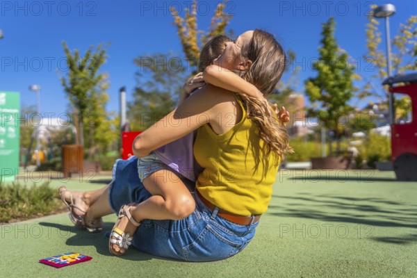 Mother and daughter embracing with affection on a soft ground surface at an outdoor playground,