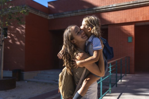 Mother holding her young daughter, both smiling and showing affection, standing outdoors near a