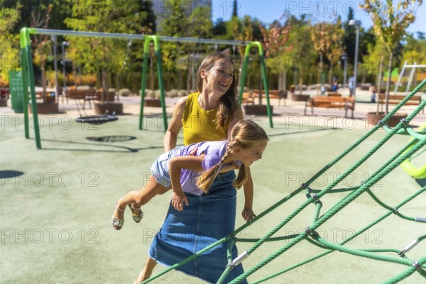 Mother and daughter smiling and laughing while playing on a sunny outdoor playground, climbing rope
