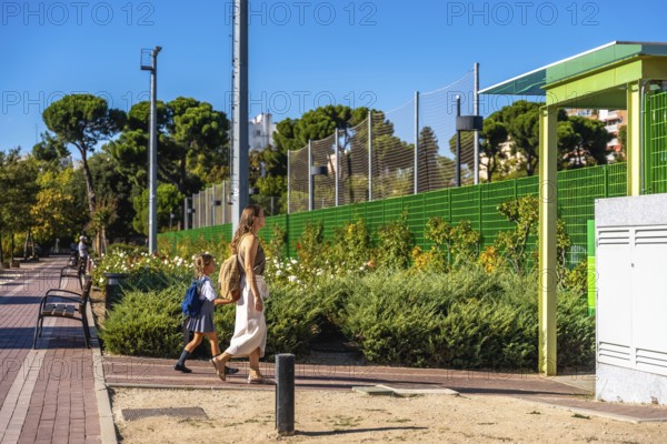 Mother and daughter walking together on a sunny day, the young student wearing a backpack and