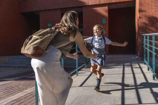 Mother and daughter joyfully reuniting for a hug outside the school building, the happy schoolgirl