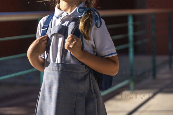 Young student in school uniform stands outdoors on a sunny day holding a backpack, ready and