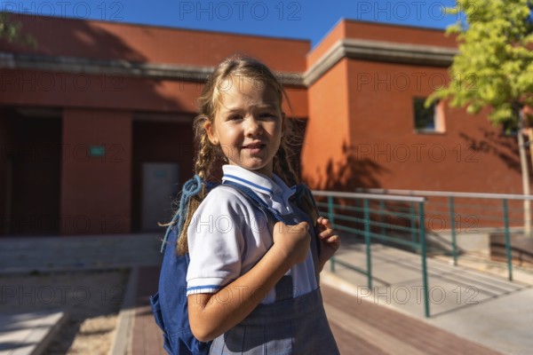 Young female student smiling and looking at the camera, wearing a school uniform and carrying a